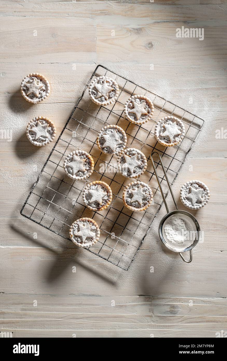 Piatto mettere mince torte sormontate con stelle di pasticceria, spolverato con zucchero a velo su sfondo bianco di legno: Natale casa cottura. Foto Stock