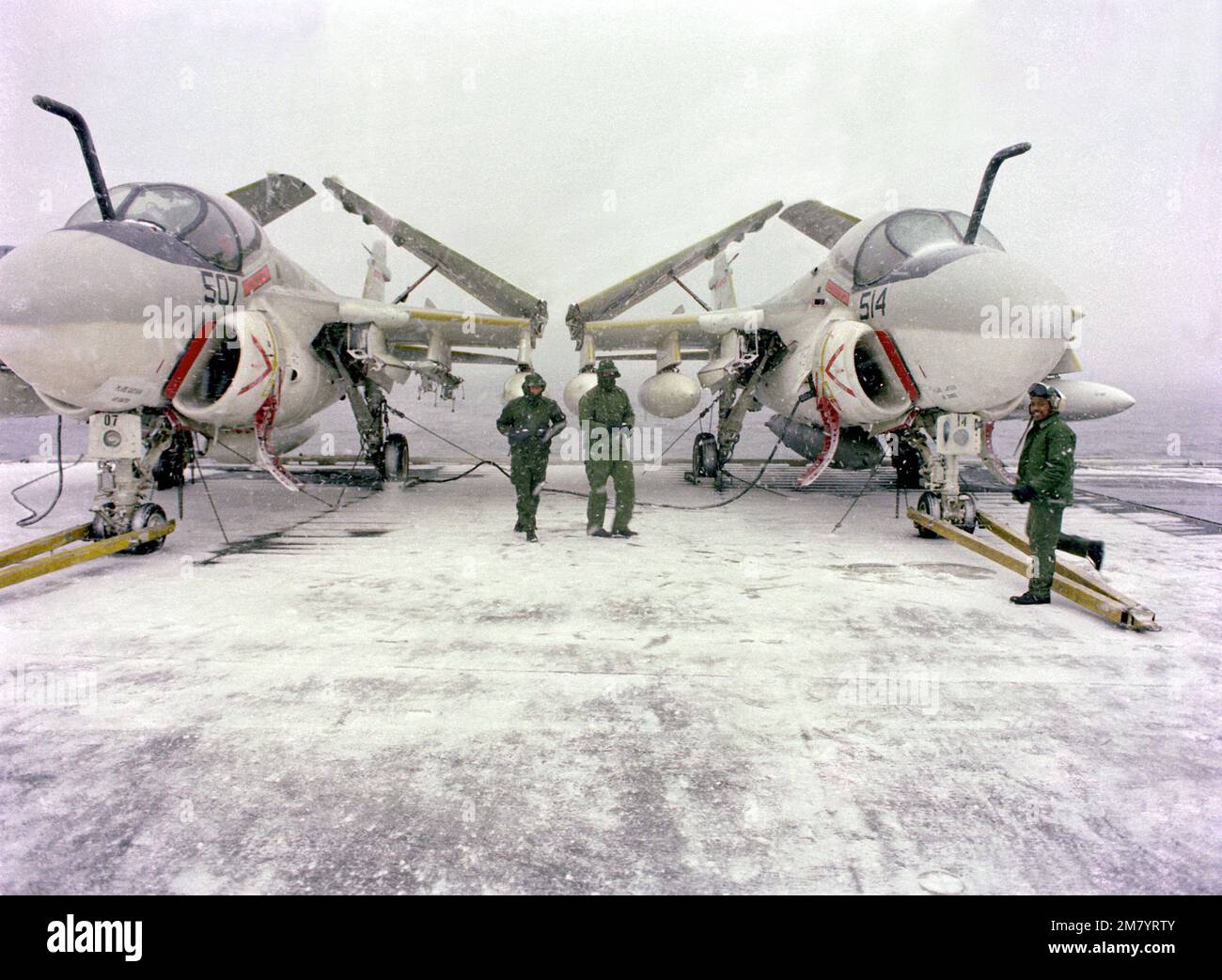 I membri dell'equipaggio del ponte di volo prestano servizio a due aerei Intruder A-6E sul ponte di volo coperto di neve della portaerei USS CORAL SEA (CV-43) durante l'esercizio NORPAC della flotta statunitense 3rd del Nord Pacifico. L'esercizio congiunto dell'aeronautica militare e della marina non solo fornisce addestramento ai piloti dei combattenti e ai controllori tattici, ma verifica anche la capacità di tali servizi di operare insieme per la difesa dell'Alaska. Soggetto operativo/Serie: NORPAC Paese: Oceano Pacifico nordoccidentale Foto Stock