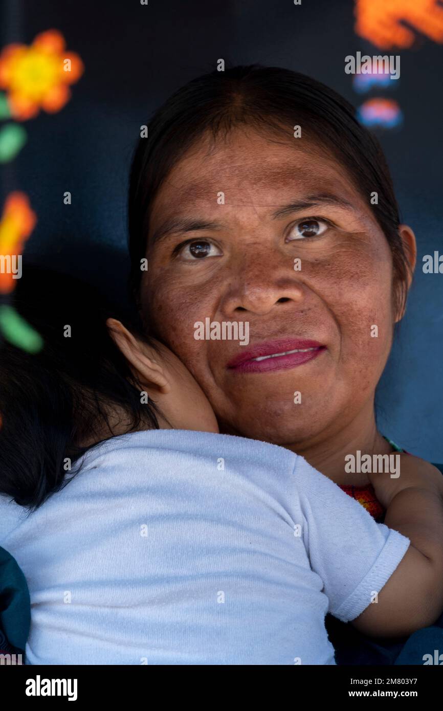 donna artigianale tradizionale che porta la figlia, circondata dal suo artigianato chaquira molto colorato Foto Stock