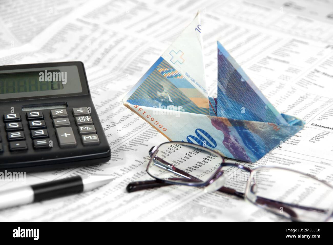 La banconota svizzera viene ripiegata a barca sulla carta con vetro oculare e calcolatrice Foto Stock