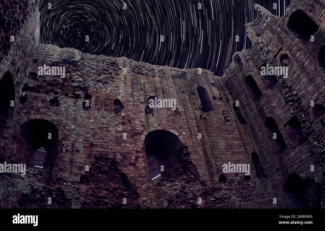 Castello di Norham in rovine con cielo notturno e sentieri stellari Foto Stock