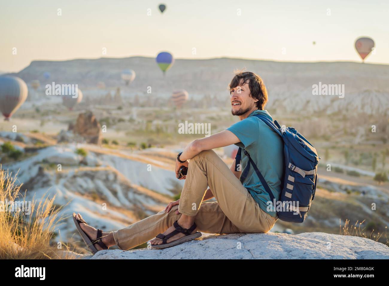 Turista che guarda mongolfiere in Cappadocia, Turchia. Buon viaggio in Turchia concetto. Uomo sulla cima di una montagna godendo di una vista meravigliosa Foto Stock