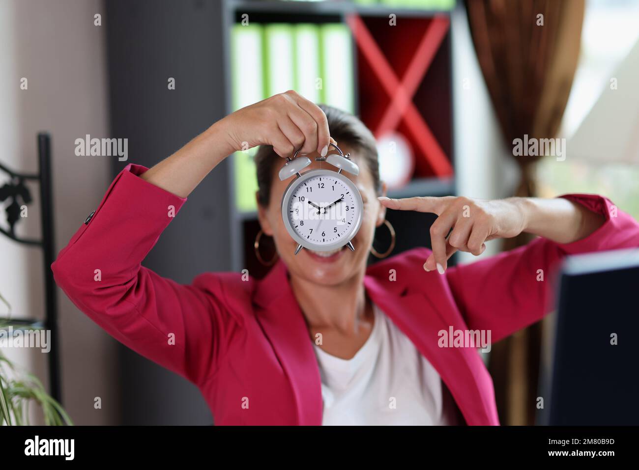 Donna in ufficio punta alla sveglia in mano. Foto Stock