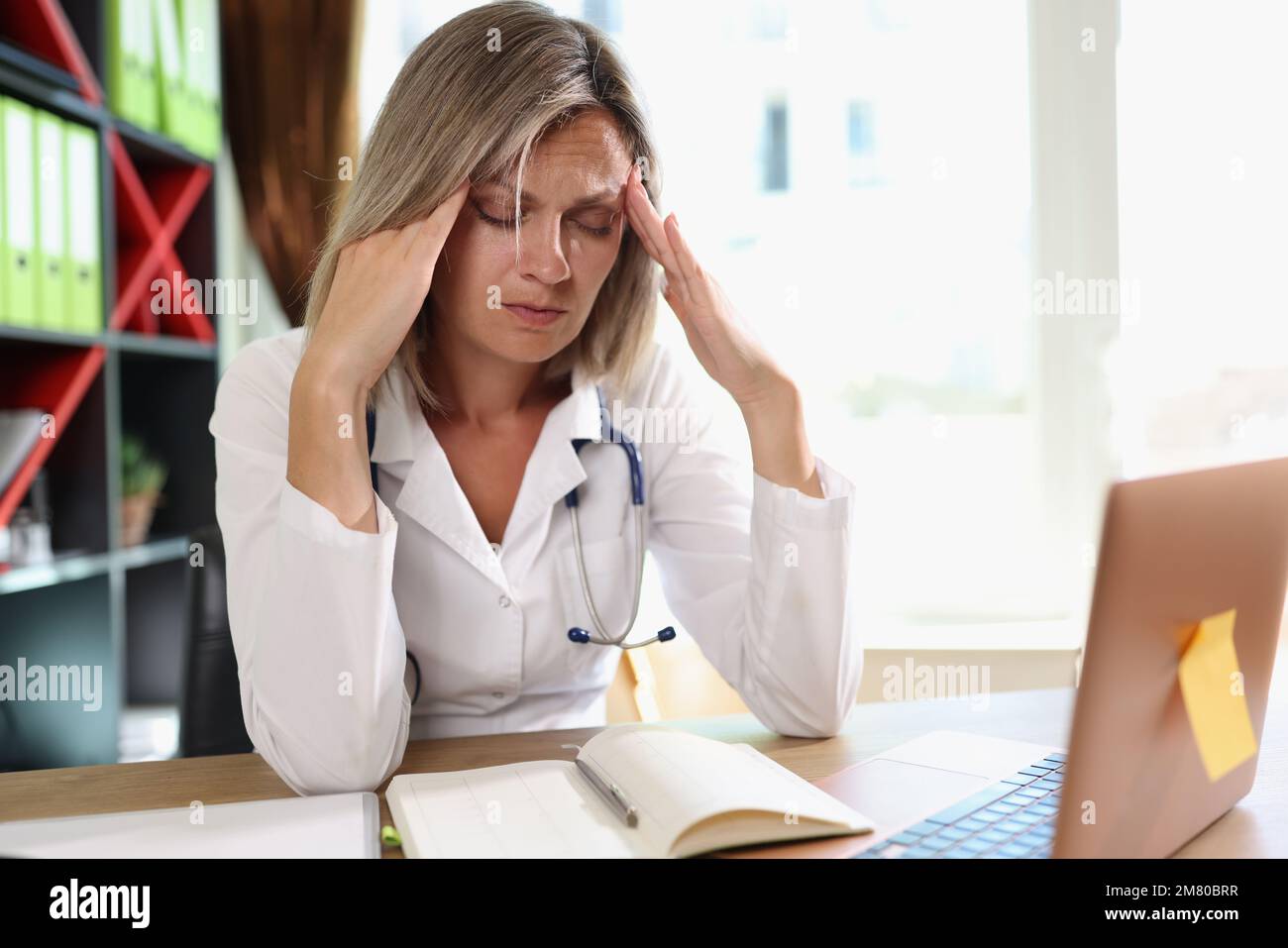 Medico di sesso femminile esausto che ha mal di testa durante il lavoro in clinica. Foto Stock