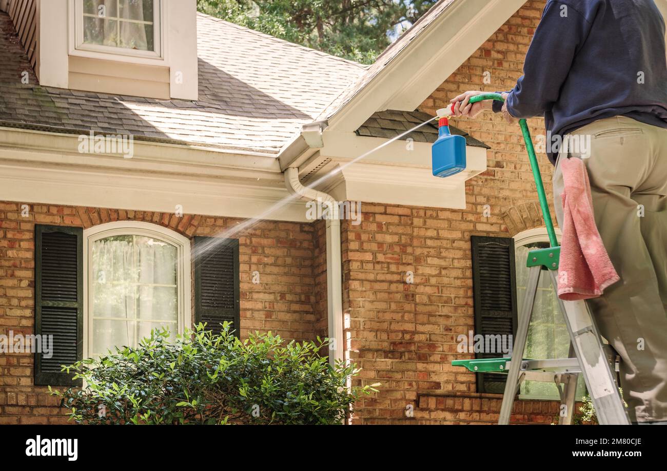 Uomo lavando le finestre della casa con uno spruzzatore di lavaggio elettrico. Servizio di pulizia con getto d'acqua ad alta pressione per pulire la facciata della casa. Foto Stock