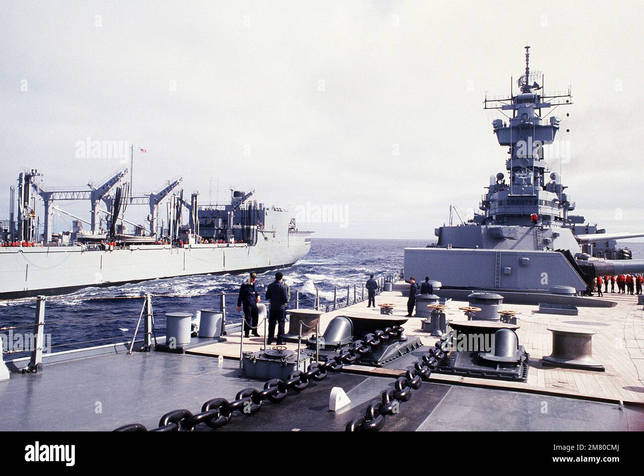 Una vista dell'area del ponte anteriore della nave da guerra USS NEW JERSEY (BB-62) con i suoi cannoni Mark di calibro 7 16 pollici/50 addestrati al porto. Un oliatore di rifornimento è in corso sul lato destro. Paese: Sconosciuto Foto Stock