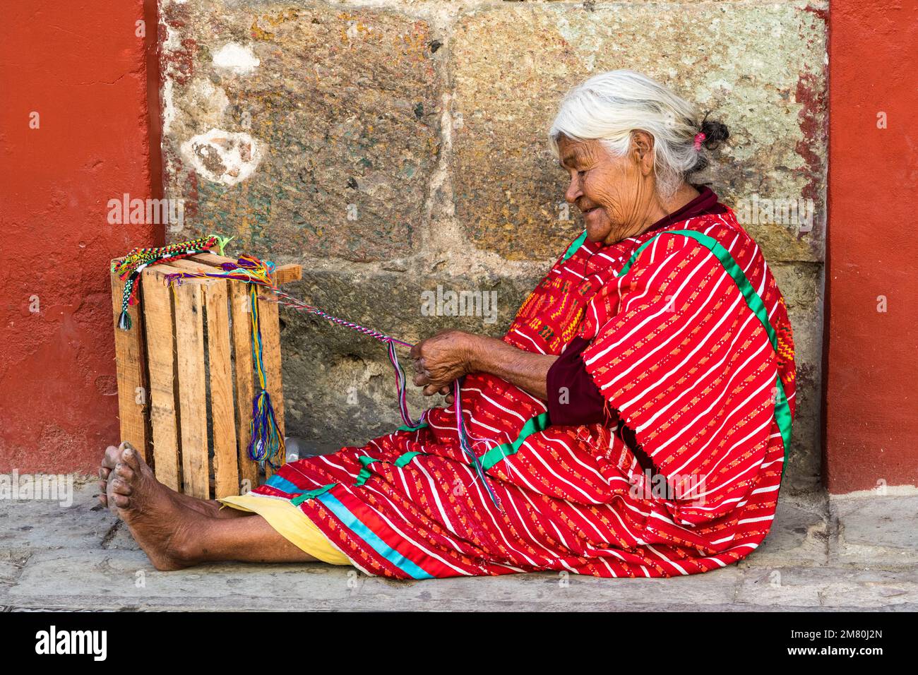 Una donna indigena indiana Trique nel tradizionale huipil intrecciato a mano che fa braccialetti sulla strada a Oaxaca, Messico. Foto Stock