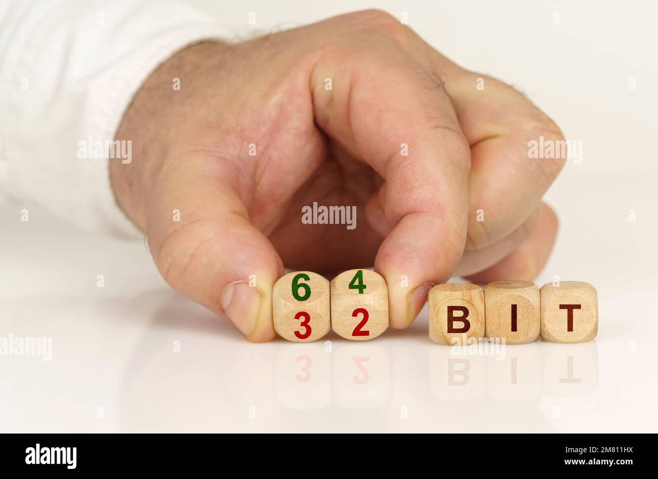 Su una superficie bianca riflettente nelle mani di un uomo sono cubi con l'iscrizione - 64 bit o 32 bit. Concetto di tecnologia Foto Stock