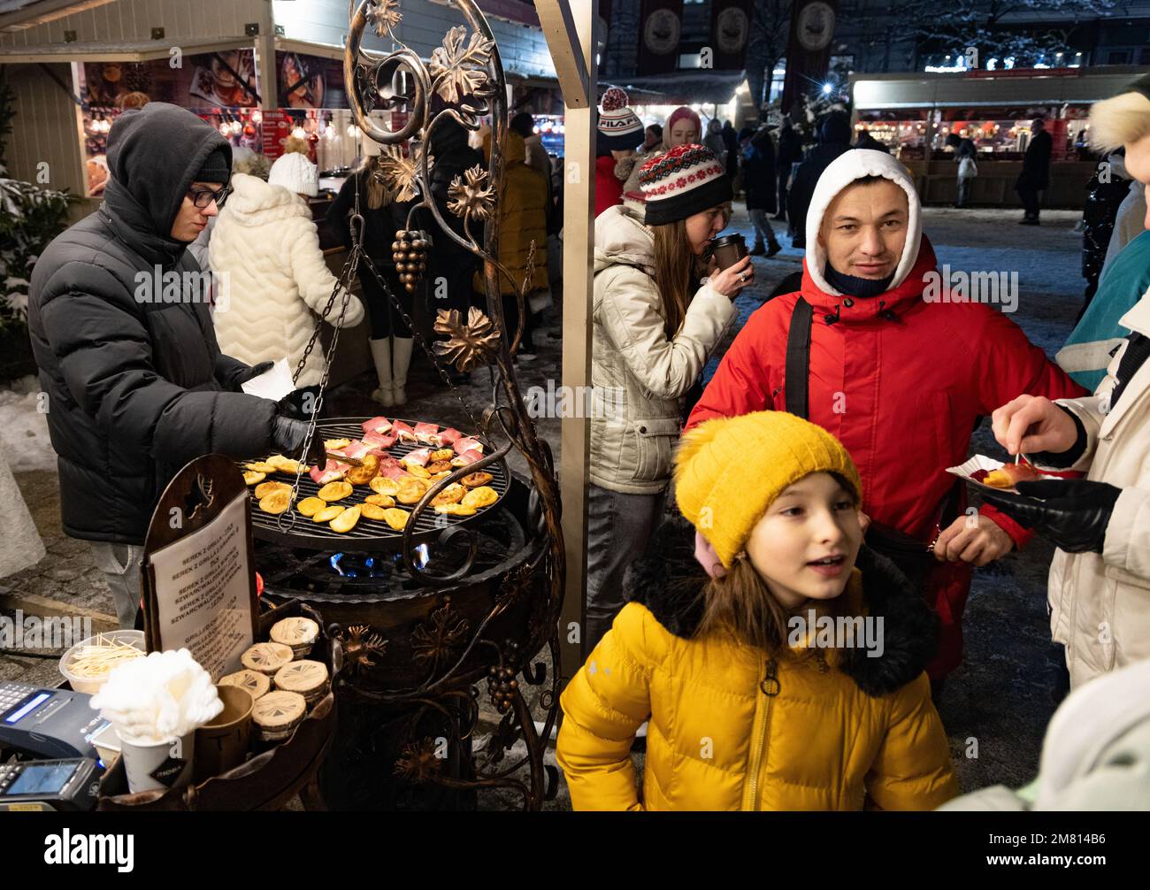 Bancarella di cibo del mercato di Natale di Cracovia; famiglia con bambini e cibo locale - formaggio di pecora con marmellata di mirtilli rossi e pancetta; Piazza del mercato principale, Cracovia Polonia Foto Stock