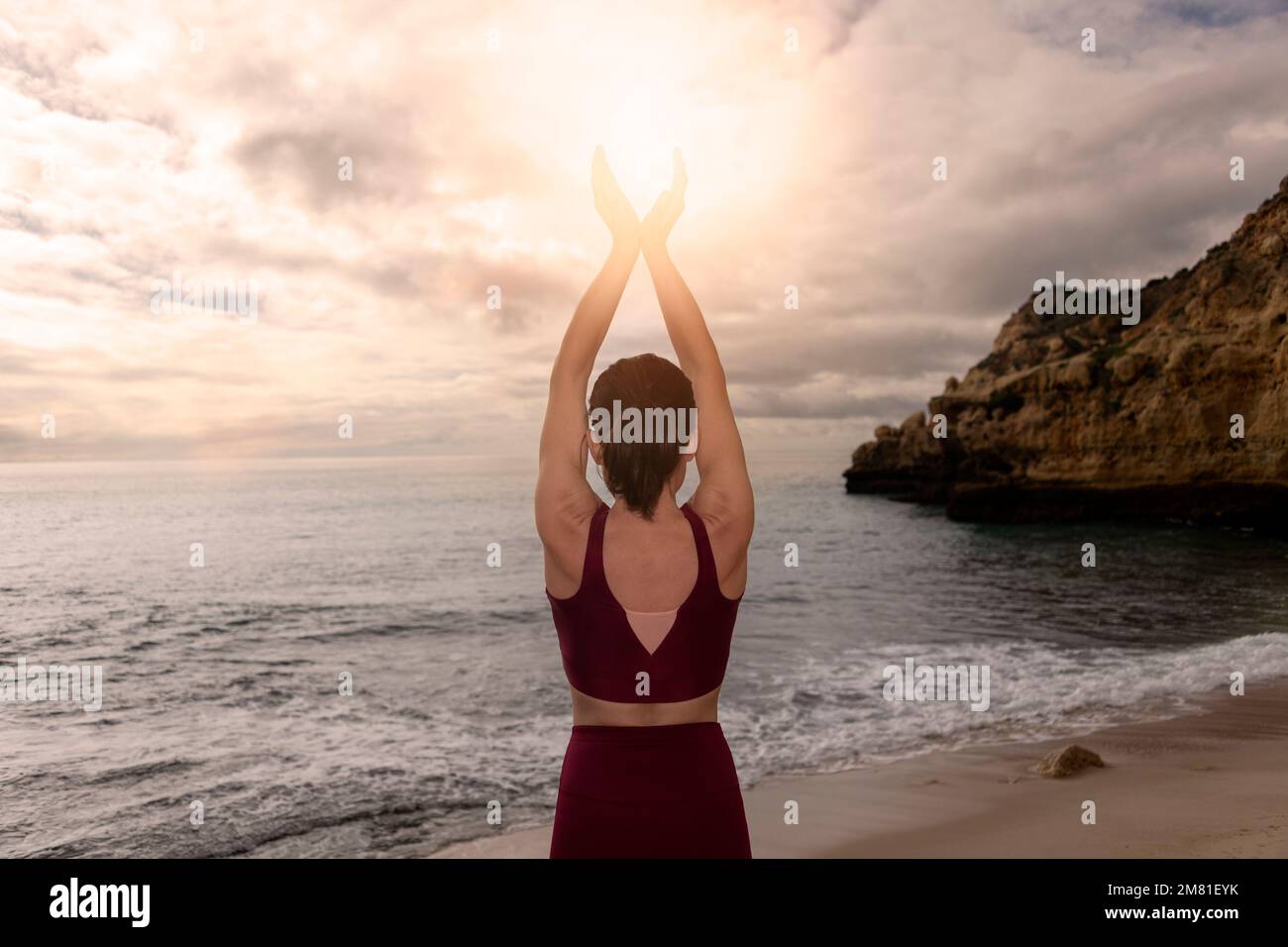 Vista posteriore di una donna meditante che coccola il sole nelle sue mani sul mare. Foto Stock