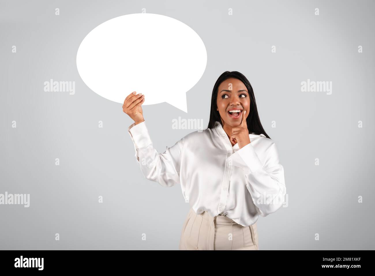 Ridendo sorpresa millenario nero donna in blusa bianca con bocca aperta tenere bolla astratta, nuvola per le parole Foto Stock