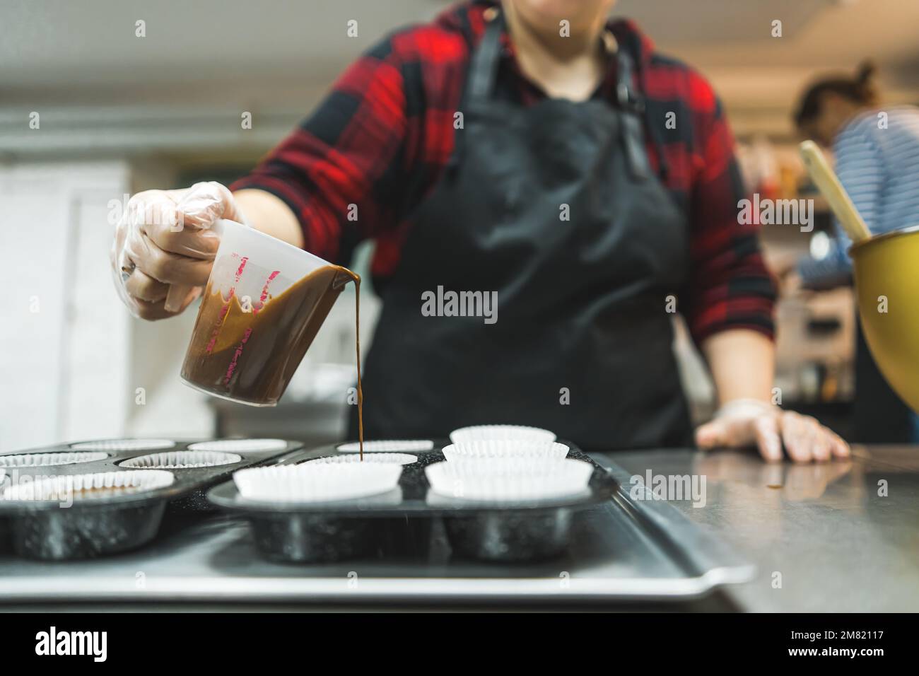 Ricetta per muffin. Stampi di carta preparati da un cuoco. Un pasticciere irriconoscibile che versa la pastella di cupcake al cioccolato negli stampi. Foto di alta qualità Foto Stock
