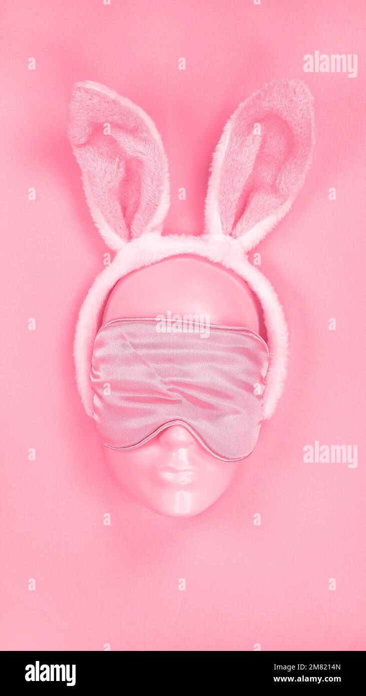 Maschera a occhio dormiente rosa sul viso manichino con soffici orecchie di coniglietto pasquale. L'immagine è colorata nel colore Viva Magenta dell'anno 2023. disturbi del sonno. Vacanze Foto Stock