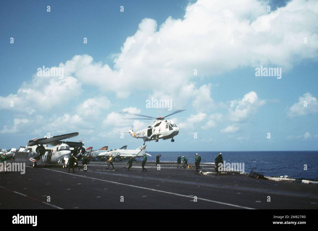 Un elicottero SH-3 Sea King solleva il ponte di volo della portaerei USS MIDWAY (CV 41) mentre un aereo commerciale C-1A si riscalda. F-4 gli aerei Phantom II sono parcheggiati sullo sfondo, a sinistra. Base: USS Midway (CV 41) Nazione: Oceano Pacifico (POC) Foto Stock