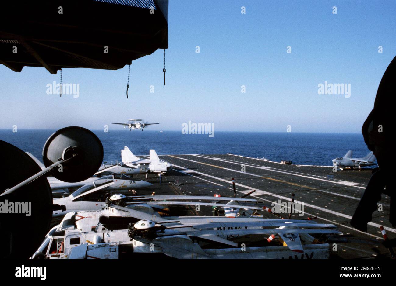 Il pilota di Landing Aid Television (PLAT), sulla stazione di telecamere dell'isola, in primo piano, viene utilizzato per registrare un velivolo e-2C Hawkeye aereo che atterra a bordo della portaerei USS JOHN F. KENNEDY (CV 67). Gli aerei Corsair II a-7 sono parcheggiati su entrambi i lati del ponte. Base: USS John F. Kennedy (CV 67) Nazione: Oceano Atlantico (AOC) Foto Stock