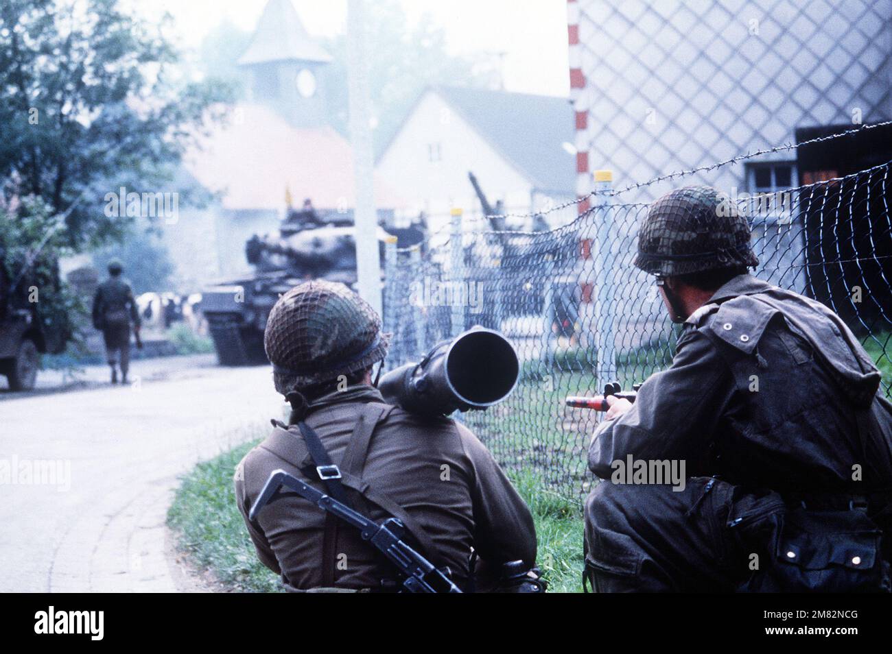I soldati olandesi armati di mitragliatrici Uzi e di una mitragliatrice Carl Gustaf 84mm M-2 osservano un convoglio di carri armati che rotolano attraverso un villaggio. I soldati partecipano a Spearpoint '84, una fase di esercizio Reforger '84. Oggetto operativo/Serie: SPEARPOINT '84REFORGER '84 Paese: Deutschland / Germany (DEU) Foto Stock