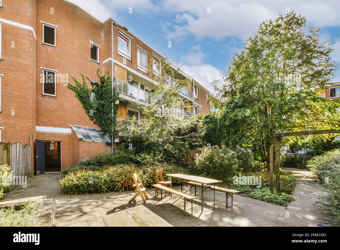un'area esterna con tavoli, sedie e alberi di fronte ad un edificio di appartamenti in mattoni in una giornata di sole cielo blu Foto Stock