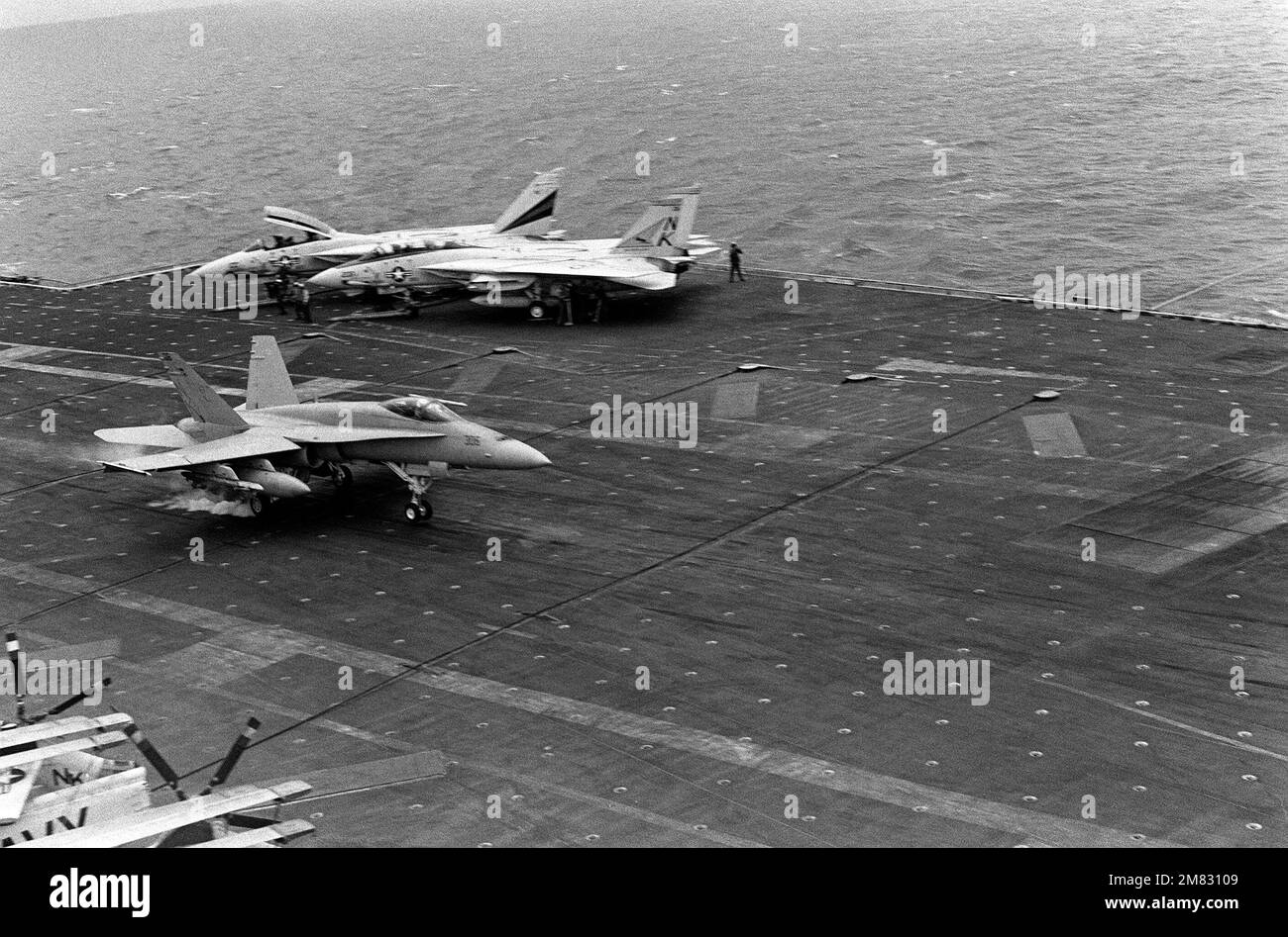 Un aeromobile F/A-18A Hornet atterra a bordo della COSTELLAZIONE USS (CV 64) della portaerei durante l'esercizio Fleet 85. Sulla destra sono parcheggiati due aerei F-14A Tomcat. Base: USS Constellation (CV 64) Nazione: Oceano Pacifico (POC) Foto Stock