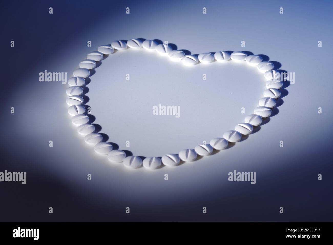 Forma del cuore di pillole bianche su sfondo bianco chiaro in blu luce dura con ombra, vista dall'alto Foto Stock