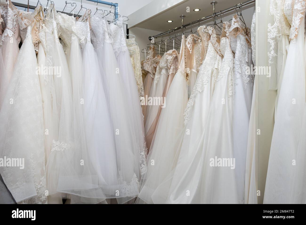 Abiti da sposa bianchi e crema su un appendiabiti in una boutique nuziale. Primo piano Foto Stock