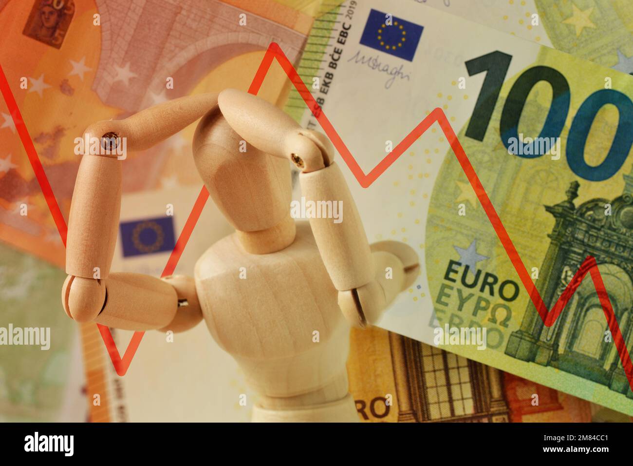 Manichino di legno con mani in testa nella disperazione e linea discendente sulle banconote in euro - concetto di crisi finanziaria e di perdita di valore monetario Foto Stock