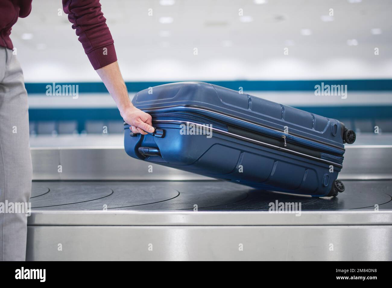 Viaggiare in aereo. Il passeggero ritira la sua valigia blu nel ritiro bagagli nel terminal dell'aeroporto. Foto Stock