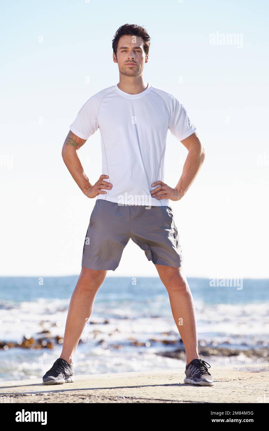Pronto per una corsa sul mare. Un giovane uomo in piedi vicino all'oceano con le mani sui fianchi. Foto Stock