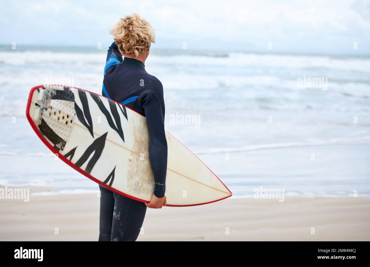 Alla ricerca del rigonfiamento... Un giovane surfista che guarda fuori sull'oceano - copyspace. Foto Stock