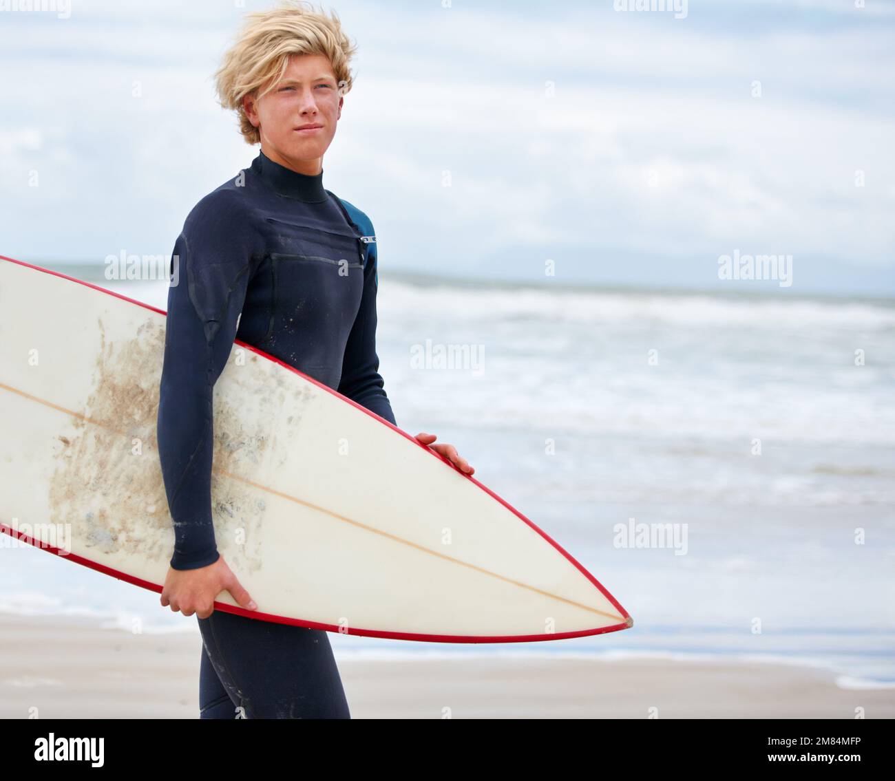 È sempre una buona giornata per fare surf. Un giovane surfista in piedi sulla spiaggia con l'oceano sullo sfondo. Foto Stock