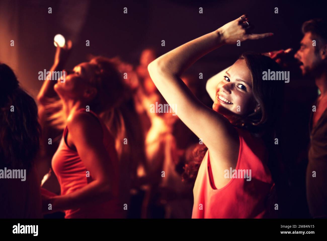 Godendo le vibrazioni al club. una giovane donna che balla con le braccia in aria con le persone sullo sfondo. Foto Stock