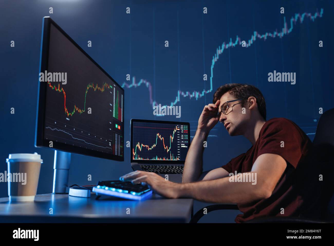 Crypto commerciante investitore guardando lo schermo del calcolatore con il grafico del candelabro in tarda notte, pensando ai rischi globali del mercato in borsa in linea, rovesciato con la recessione globale e la perdita di soldi Foto Stock