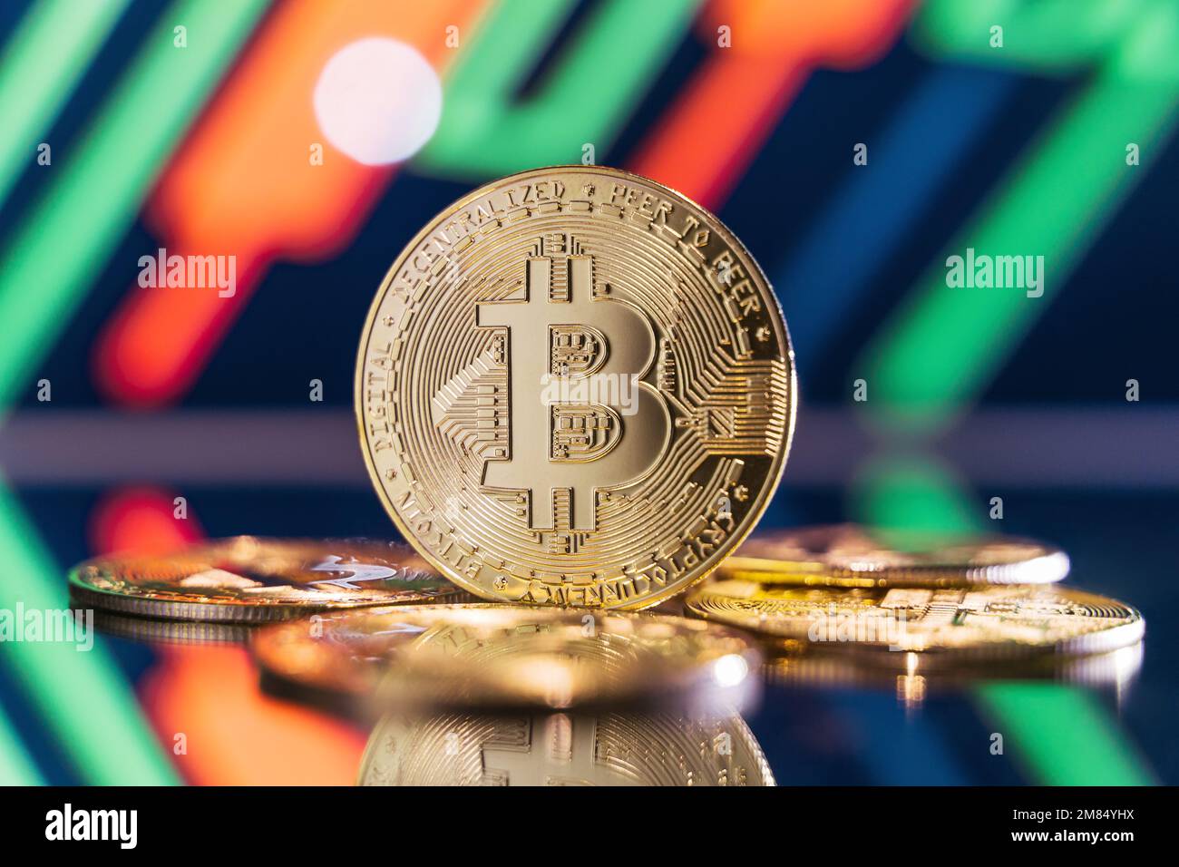 Bitcoin dorato in piedi sulla superficie a specchio che riflette sfondo sfocato con carta cripto con candelabri verdi e rossi. Concetto di mercato della criptovaluta Foto Stock