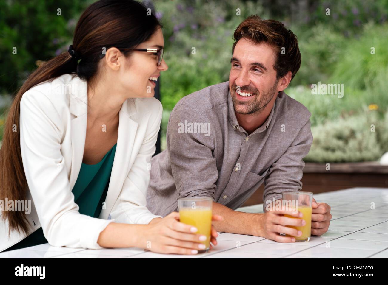 Un paio di colleghi felici che parlano in piedi alla finestra dell'ufficio con il succo. Foto Stock