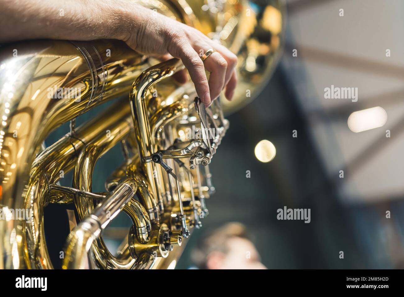 La mano di un uomo è vista suonare un grande tuba strumento di ottone come parte di un'orchestra durante una cerimonia. Faccia non mostrata. Concetto di musica, performance o celebrazione. Foto Stock