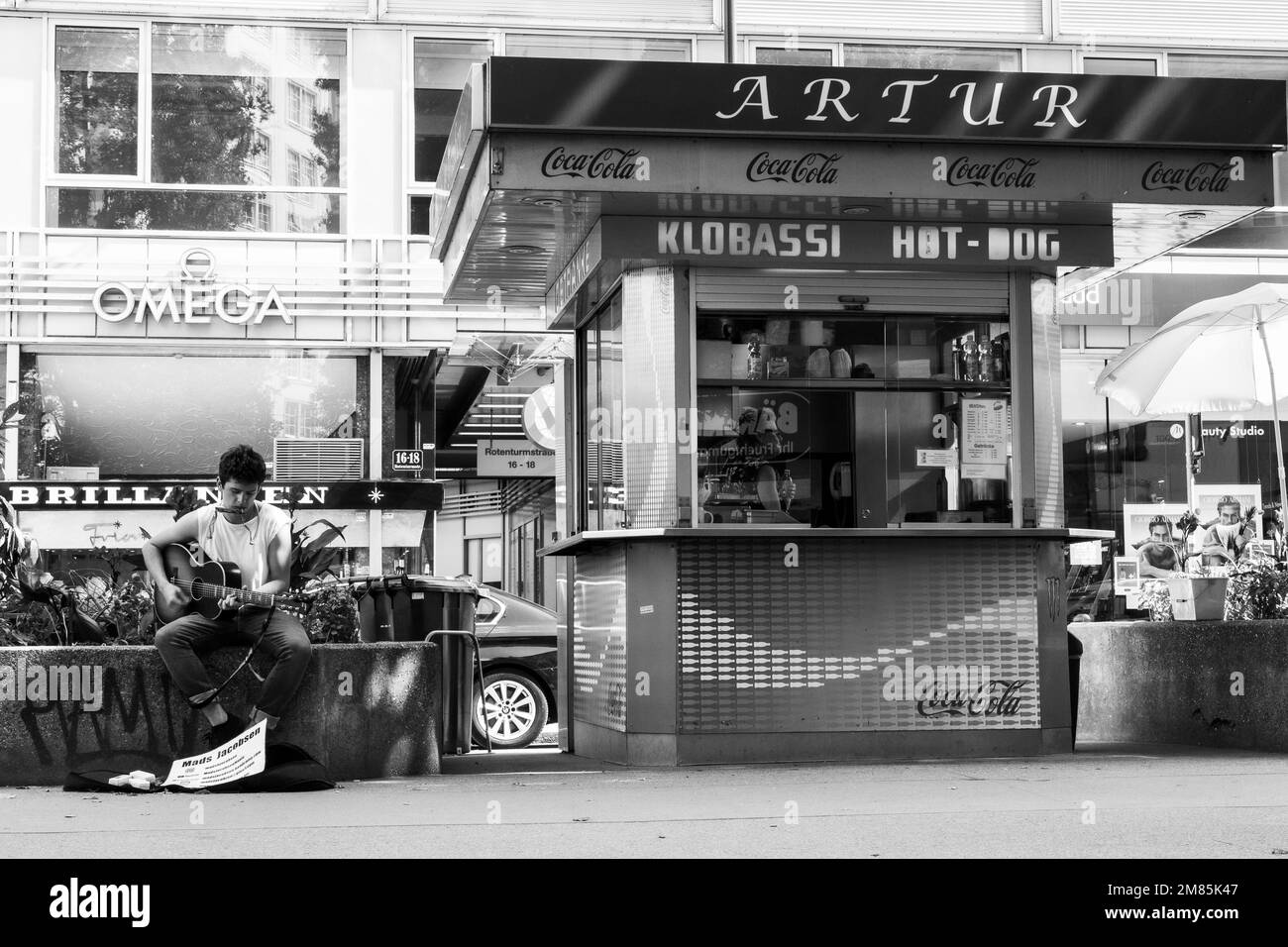 Mads Jacobsen, busker, suonando la chitarra seduto sul muro vicino allo stand hotdog sulla Rotenturmstrasse a Vienna mentre la coppia compra il pranzo Foto Stock