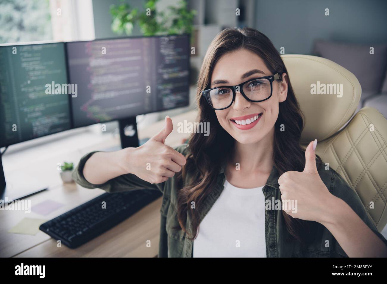 Foto di felice allegro signora content maker indossare occhiali smilig che mostra due pollici su workshop interno workstation Foto Stock