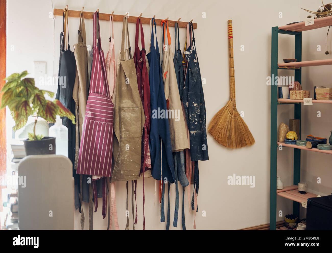 Appendiabiti, grembiule e dipingere con una scopa in un laboratorio vuoto o studio contro il muro della vita morta per il design. Creatività, arte e abbigliamento con un gruppo Foto Stock