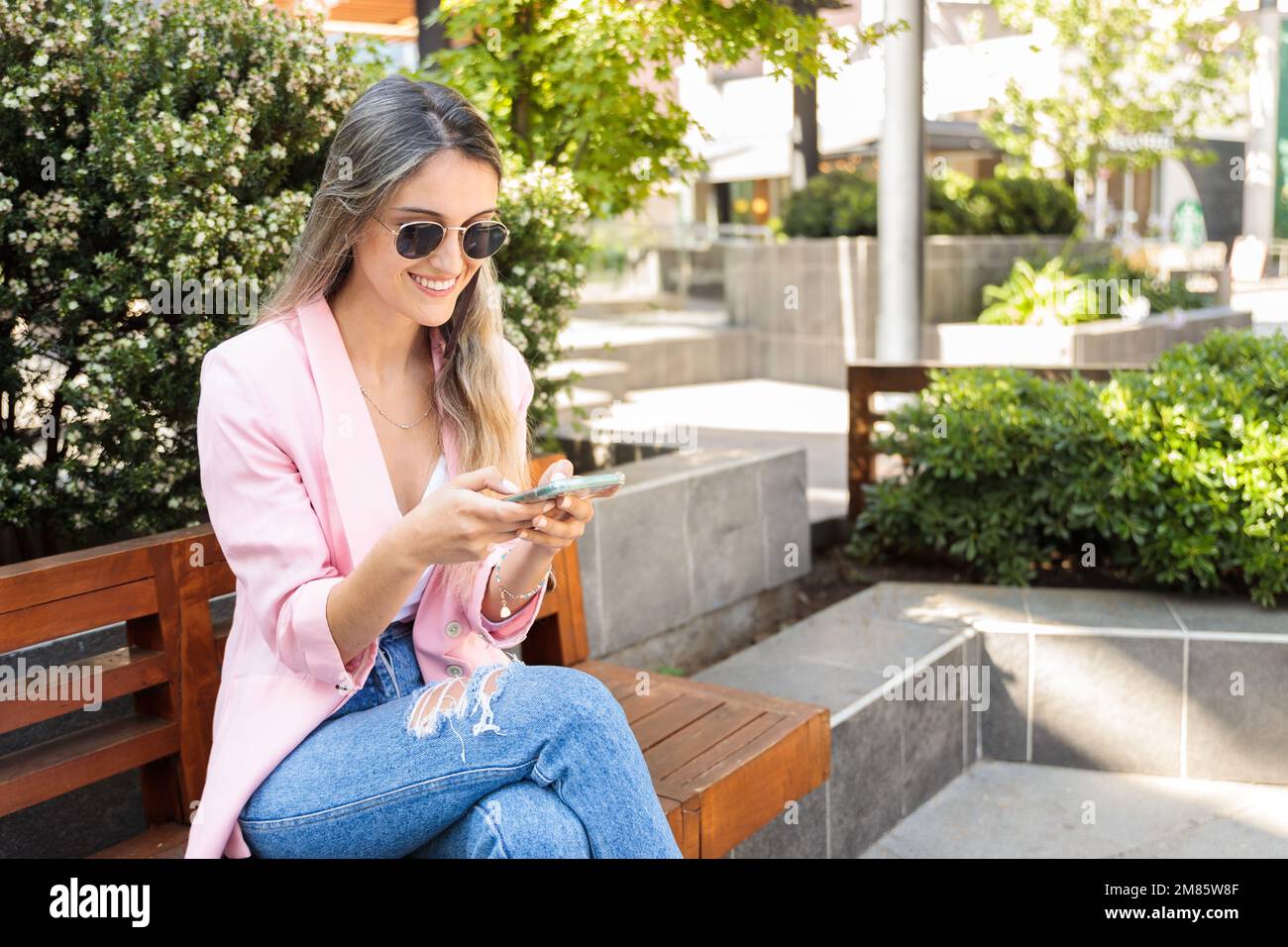 Giovane donna sorridente che usa lo smartphone fuori dal centro commerciale. Dipendenza da Internet e dai social media Foto Stock