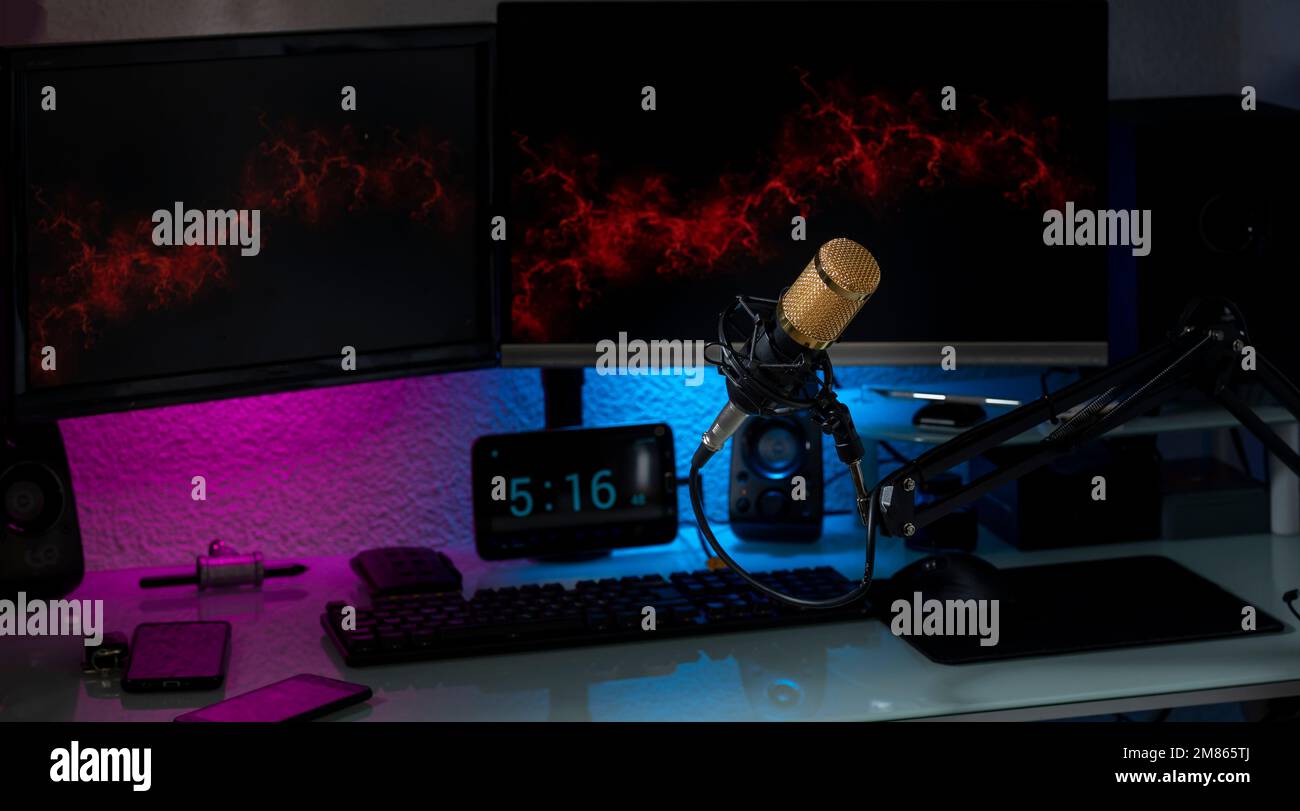 Microfono a condensatore in configurazione gamer con monitor, tastiera, mouse e luci colorate. Foto Stock