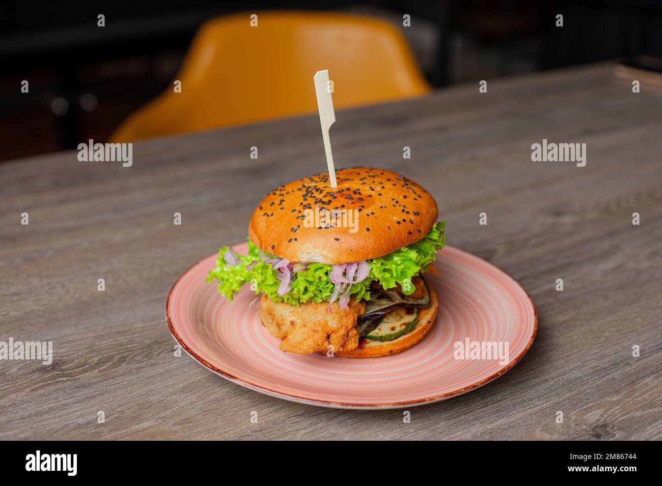 Primo piano con succulento appetitoso hamburger di pollo isolato su sfondo tavolo di legno. Servizio di panino calorico grande su spiedino. Fast food cafe Foto Stock