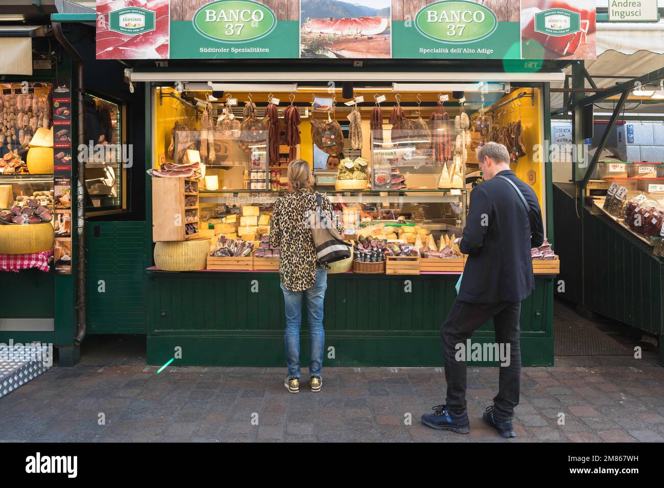 Mercato di Bolzano, vista delle persone che acquistano cibo da una stalla specializzata in carni e formaggi locali nel mercato di Piazza Erbe, centro di Bolzano, Italia Foto Stock