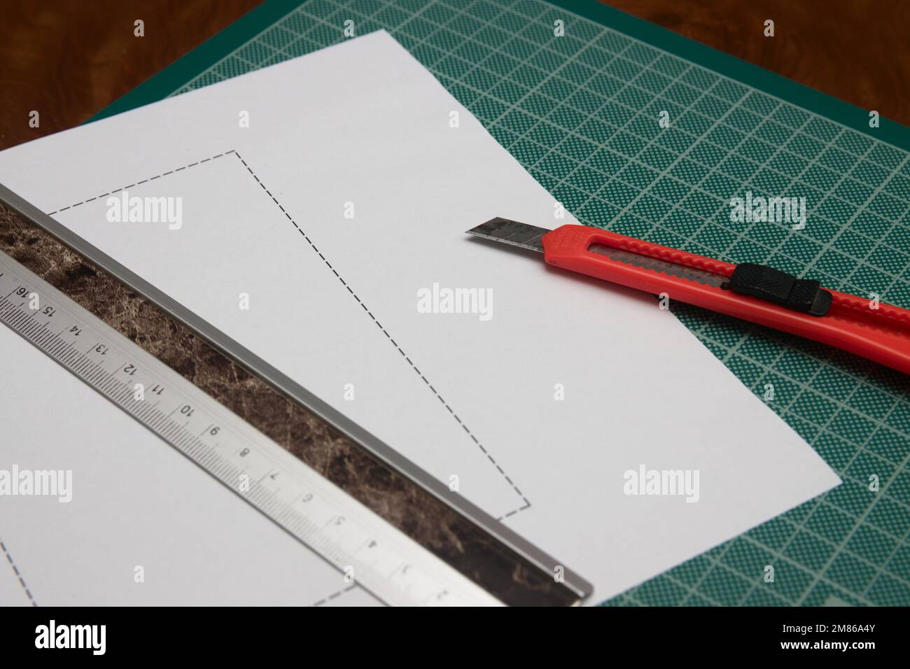 Qualcuno che taglia una carta con l'aiuto di un taglierino e di un righello su un tavolo di lavoro verde Foto Stock Qualcuno che taglia una carta con l'aiuto di un taglierino e di un righello su un tavolo di lavoro verde Foto Stock