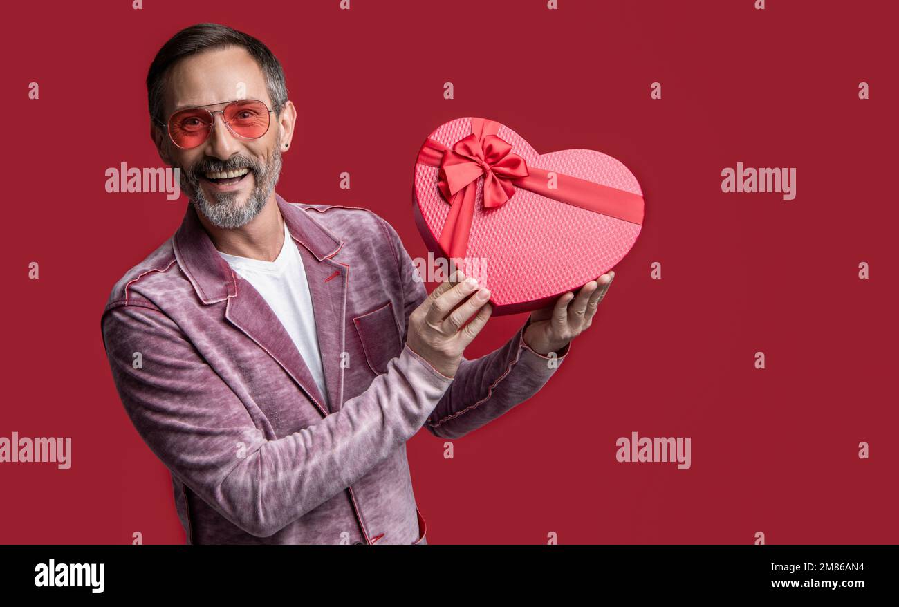 foto dell'uomo maturo che mostra il dono di san valentino. uomo maturo con  regalo di san valentino isolato sul rosso Foto stock - Alamy