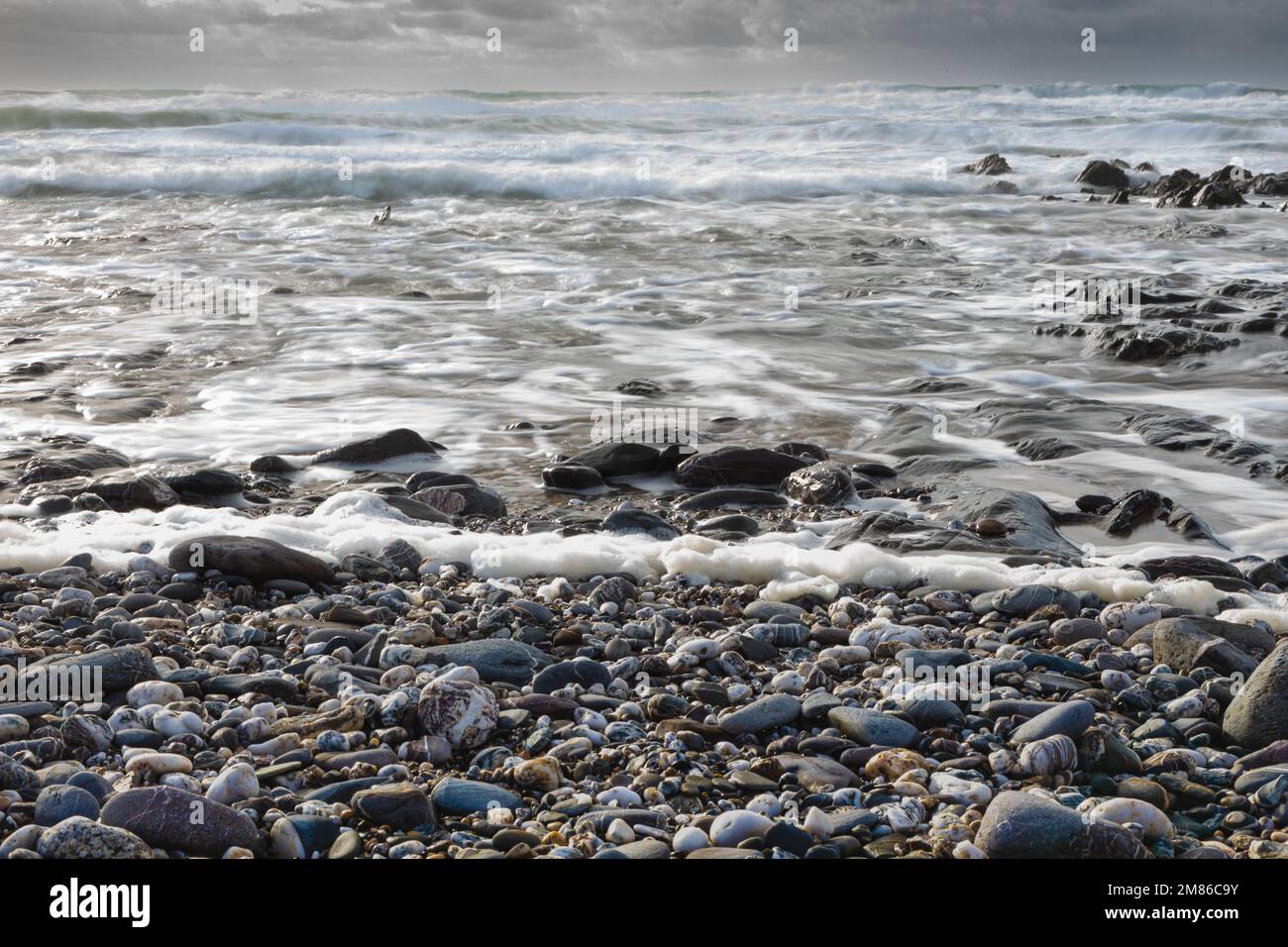 Ciottoli lisci sul bordo delle acque con onde e mare che si avvicinano Foto Stock