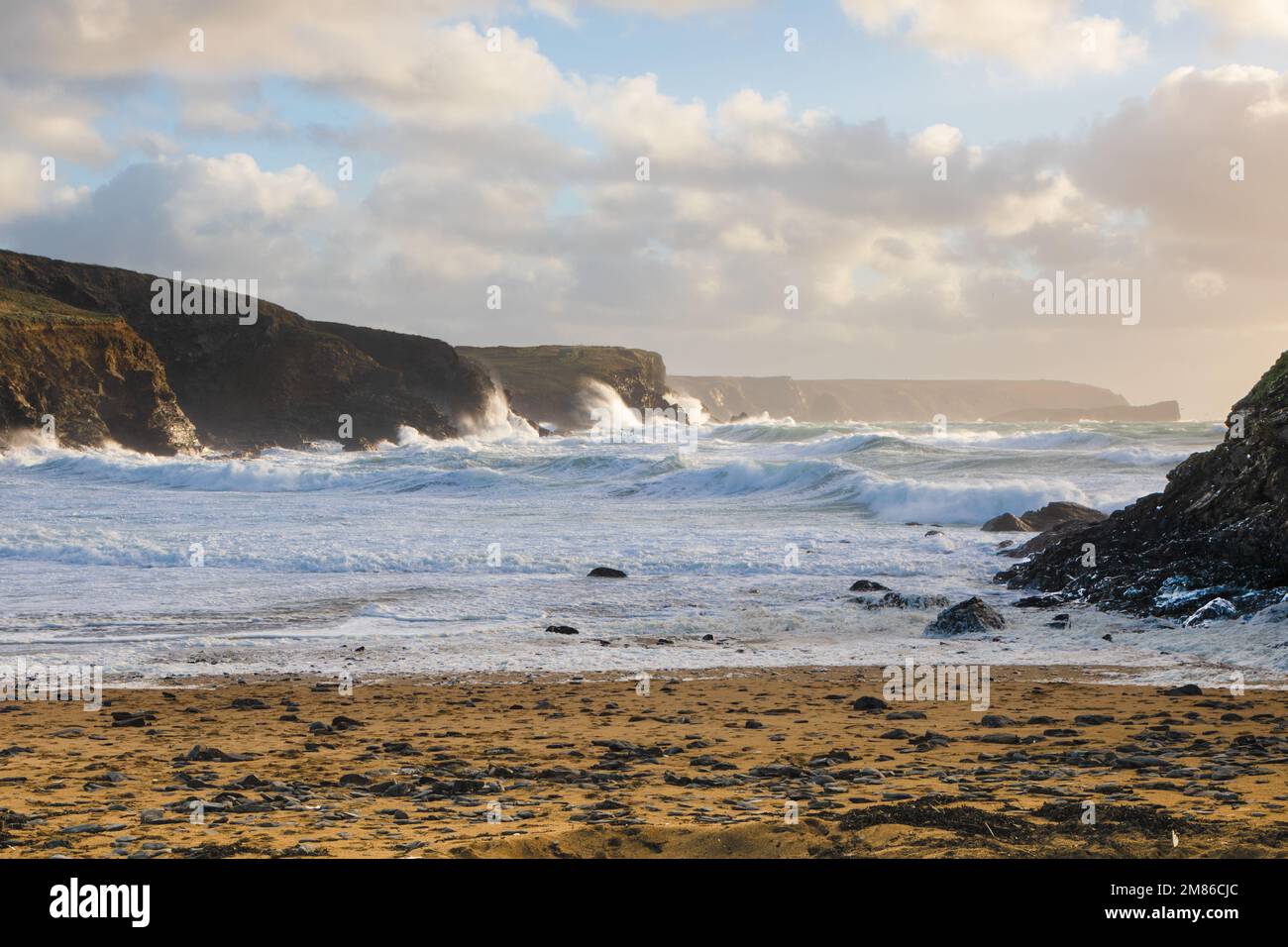 Scena di mare che mostra l'acqua di mare bianca frothy che rotola su una spiaggia e le onde che si schiantano contro le rocce a Dollar Cove, il Lizard, Cornovaglia con un nuvoloso Foto Stock