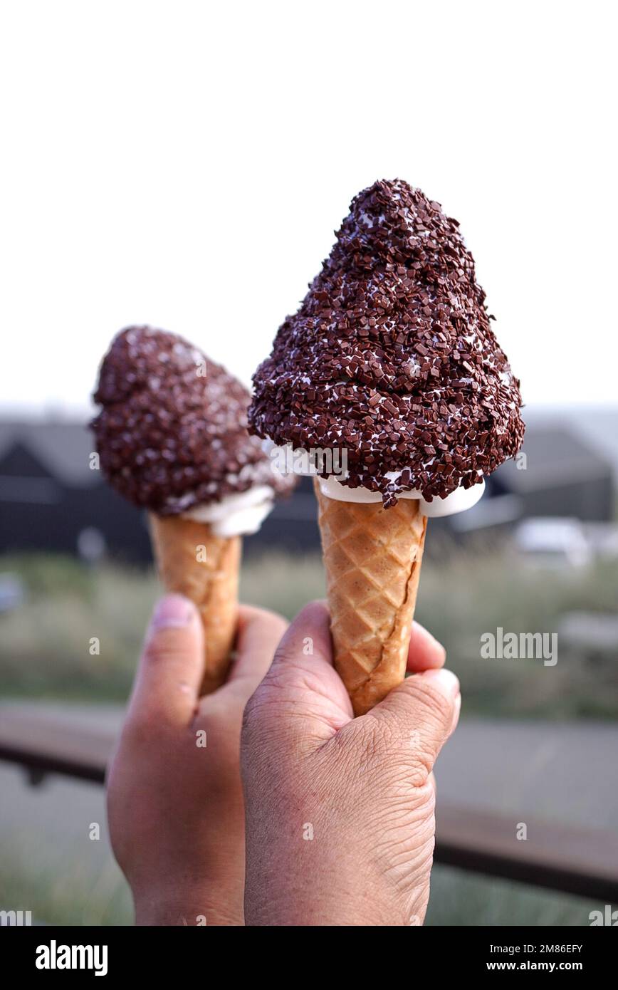 Un colpo verticale di mani che tengono coni di gelato ricoperti di gocce di cioccolato Foto Stock
