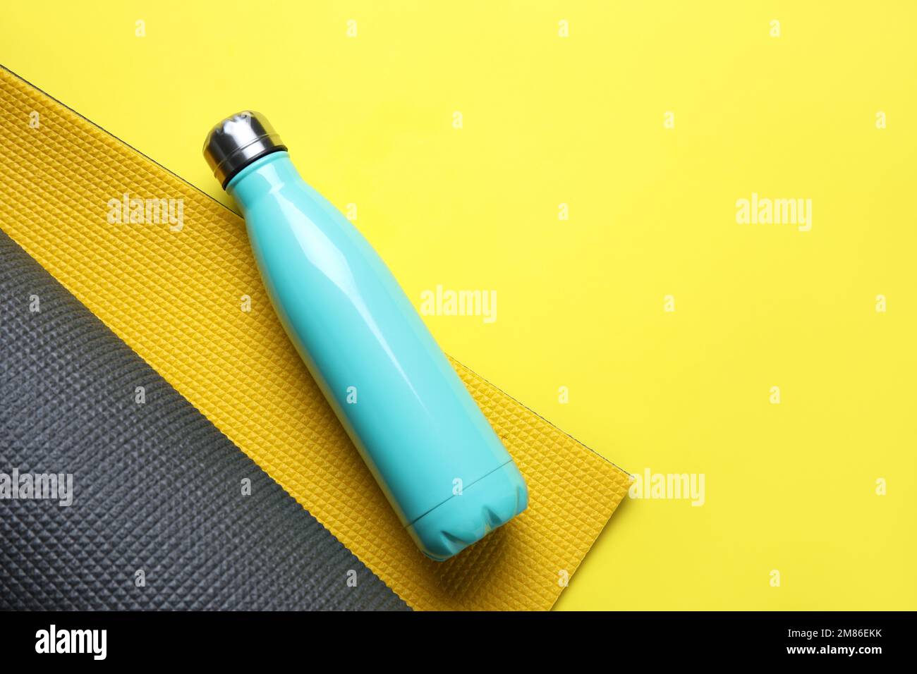 Bottiglia d'acqua sportiva con tappetino fitness su sfondo giallo Foto Stock