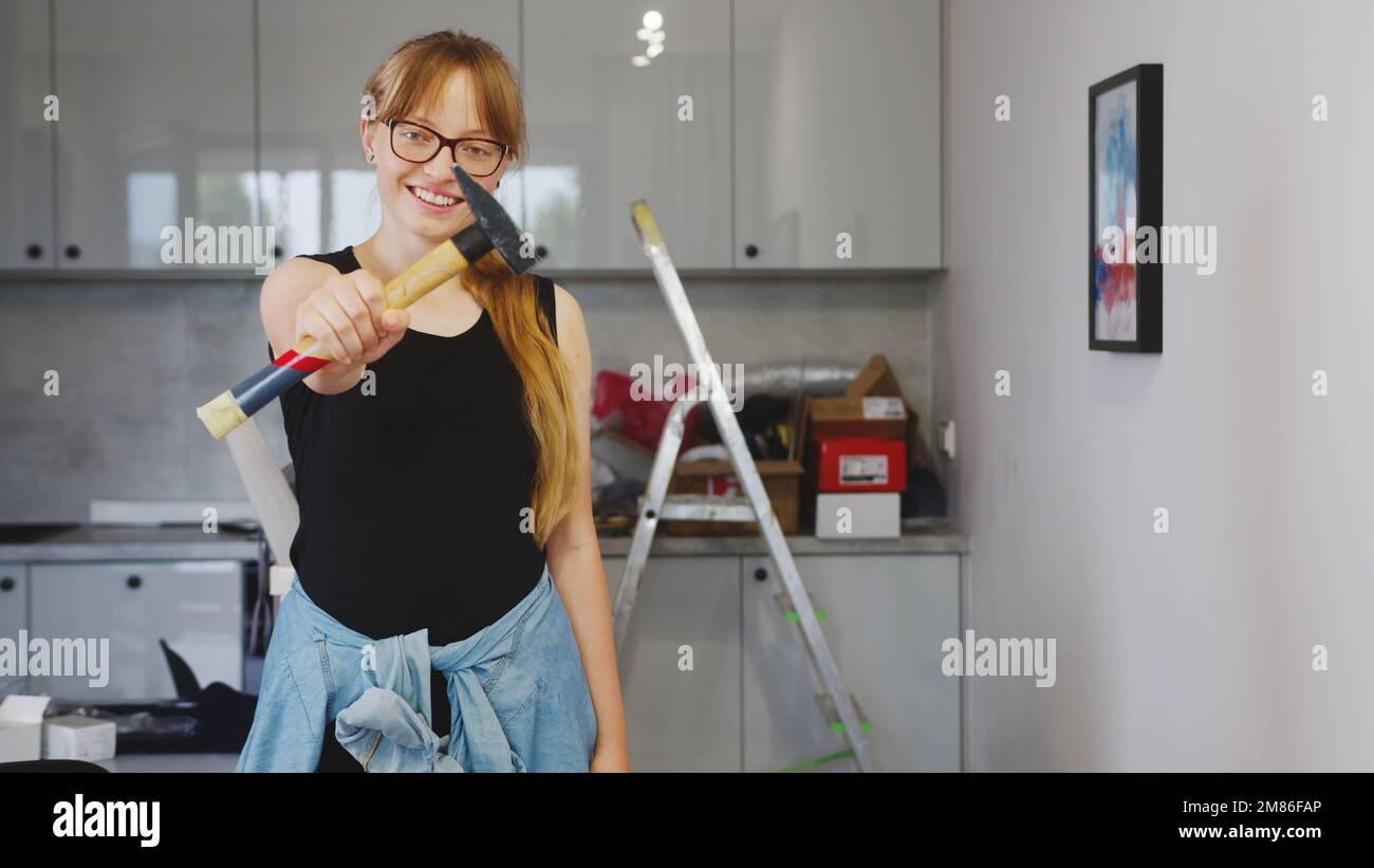 Giovane donna caucasica con lunghi capelli biondi mostrando un martello alla macchina fotografica, tiro medio cucina riparazione concetto. Foto di alta qualità Foto Stock
