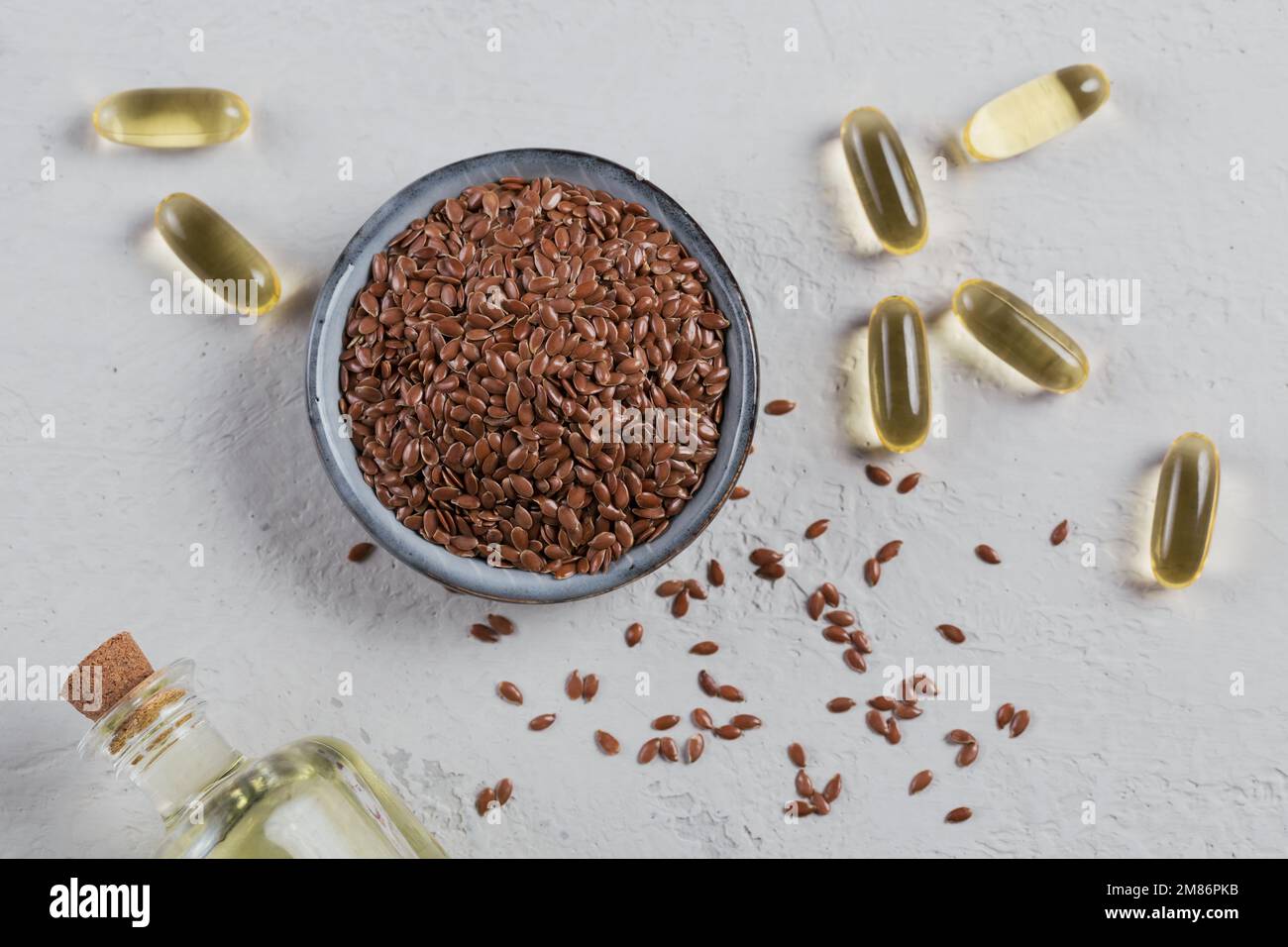 Rosolare i semi di lino o di lino in ciotola piccola e capsule di gelatina con olio di lino su fondo grigio chiaro. Foto Stock