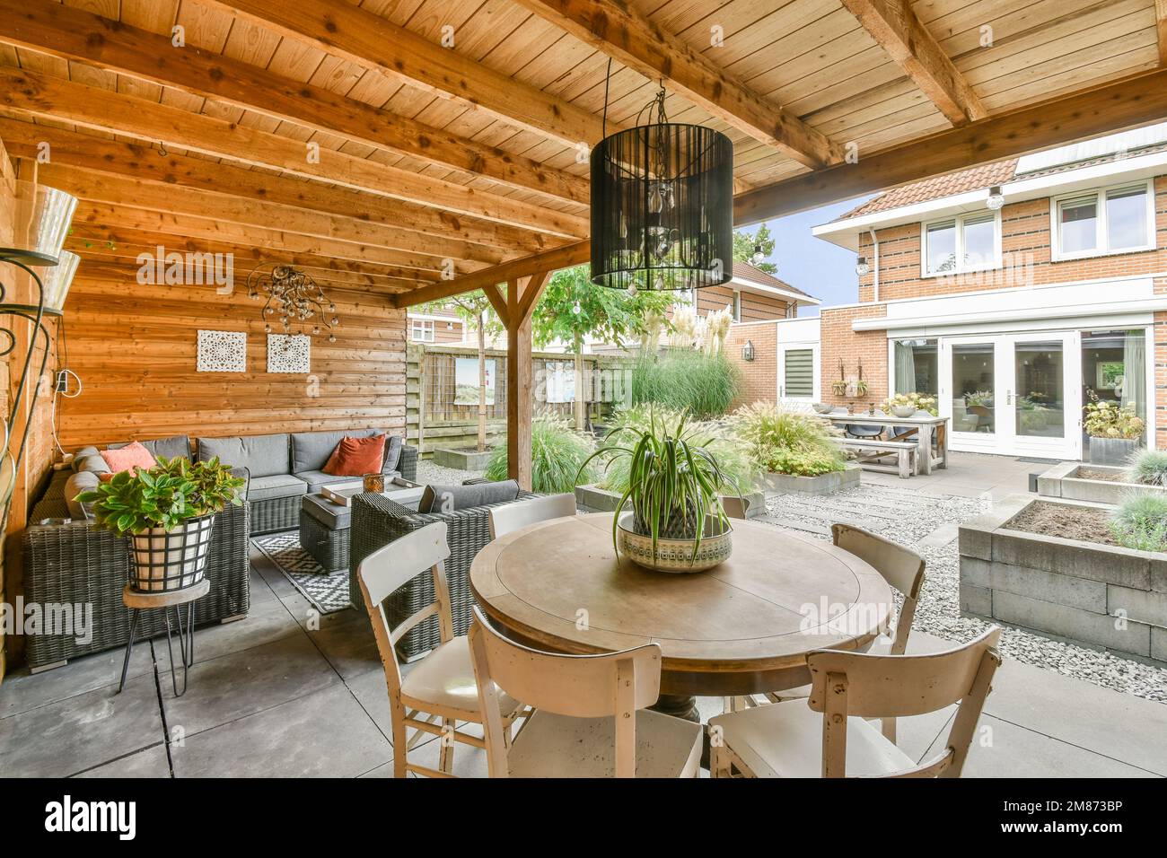 un patio con sedie, tavoli e piante sul tavolo di fronte ad un soggiorno all'aperto che ha pareti in pannelli di legno Foto Stock
